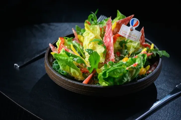 A salad garnished with sliced dry-cured pork.