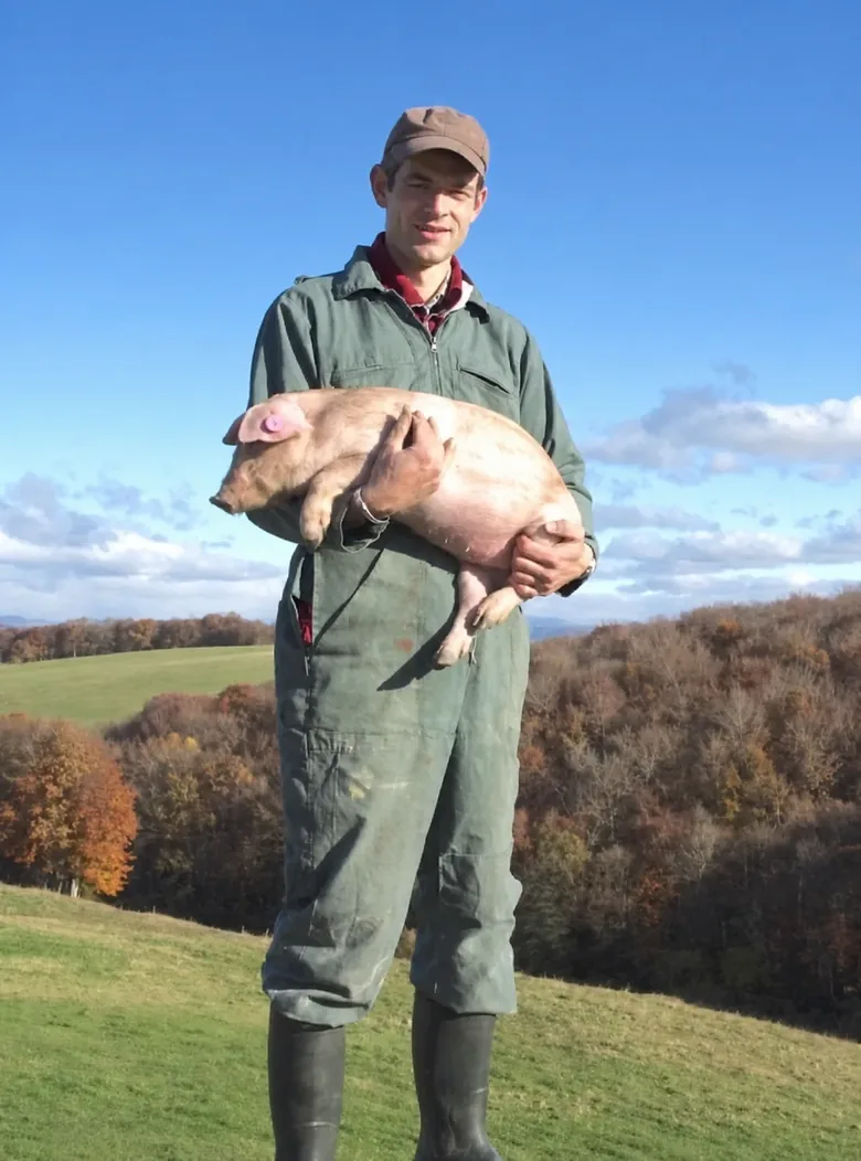 A farmer holding a piglet in a mountain field.